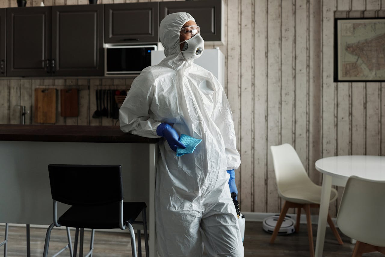A person in full PPE gear standing indoors, emphasizing disinfection during COVID-19.